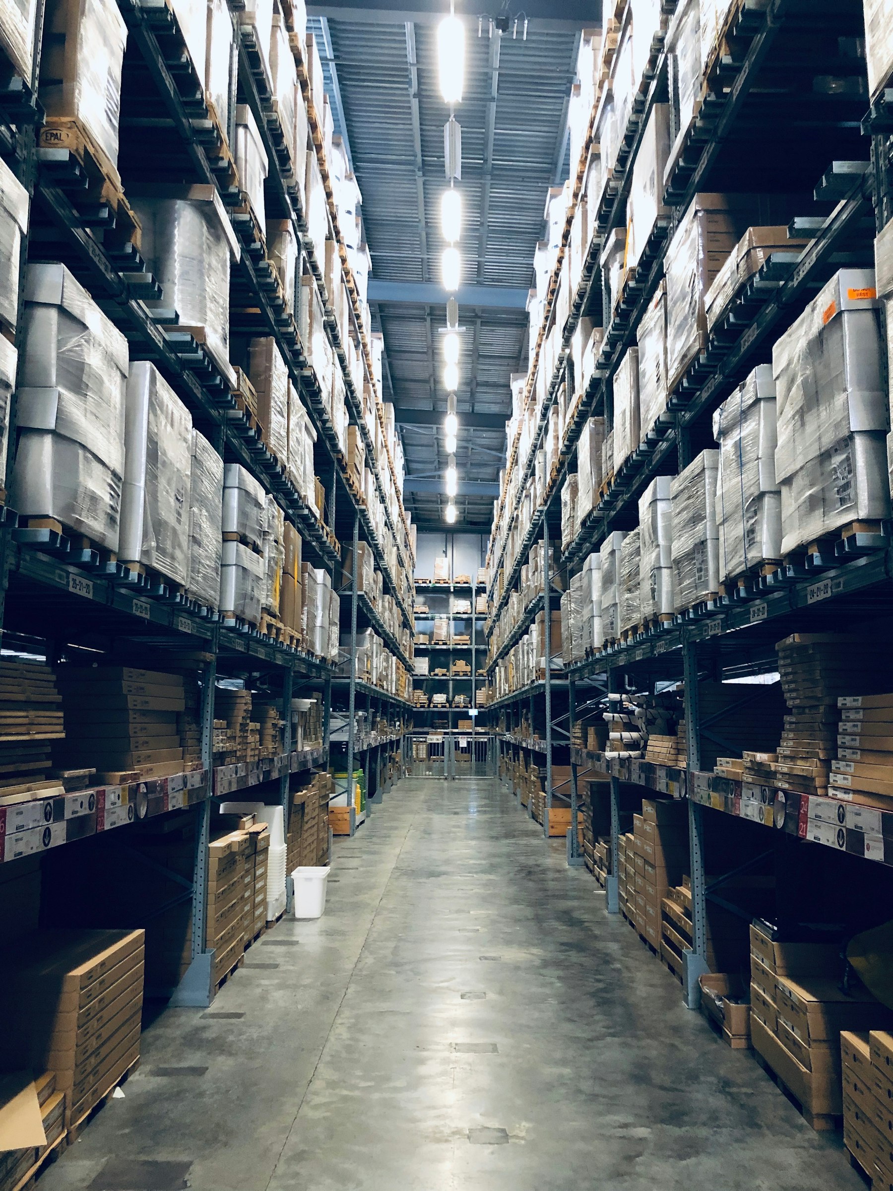 廠內高聳料架走道，鋼鋁料件分層堆放排列整齊，第二廠鋁鐵料整合
